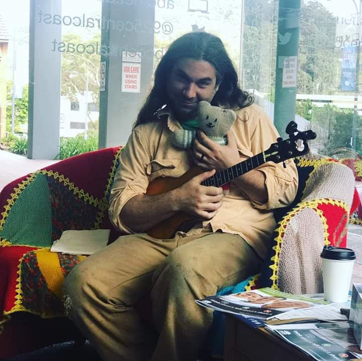 Russ relaxing in a colorful chair with a ukulele and a stuffed koala