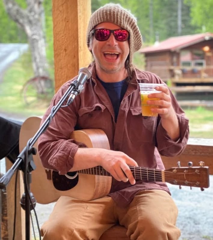 Ukulele Russ smiling with a drink, microphone and guitar