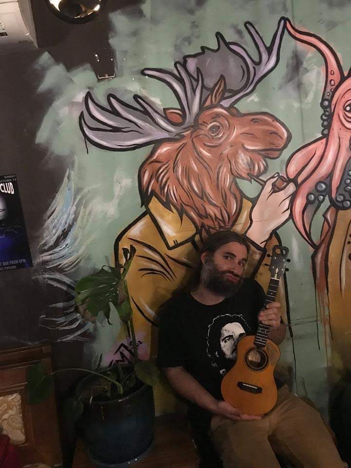 Ukulele Russ posing beside a colorful moose mural