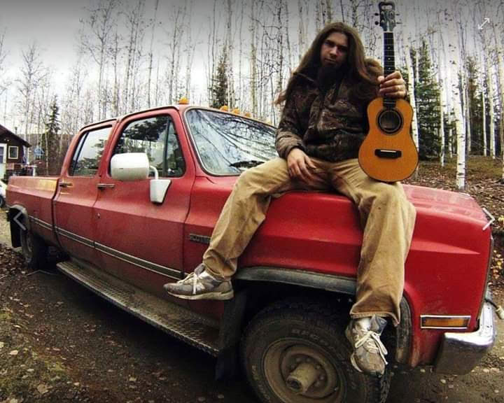 Ukulele Russ sitting on a red truck in Alaska