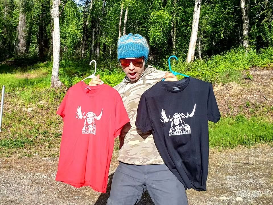 Ukulele Russ holding red and black handmade shirts